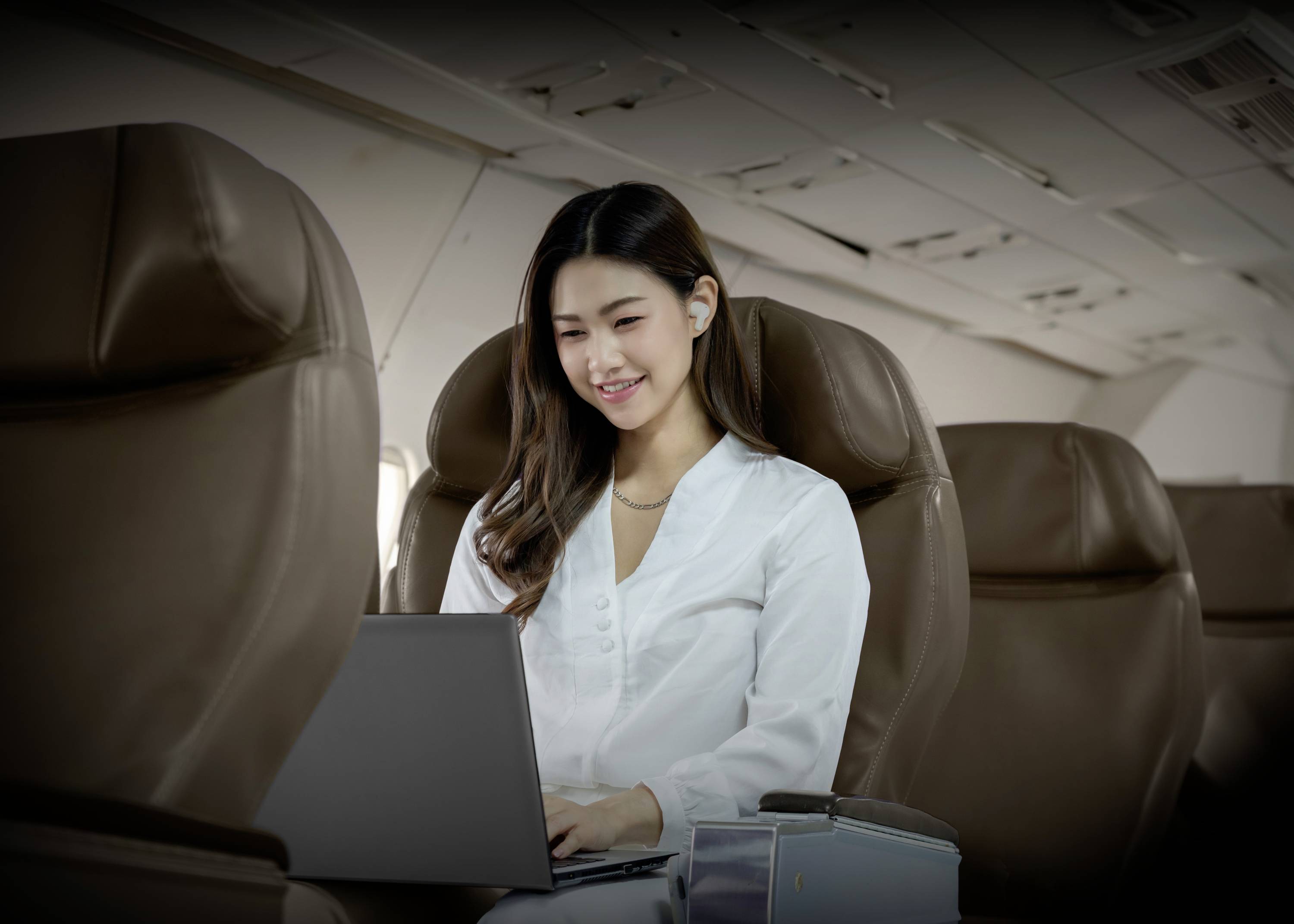 Frau arbeitet mit Laptop im leeren Flugzeug, trägt weiße Kleidung, Fokus auf Bildschirm.