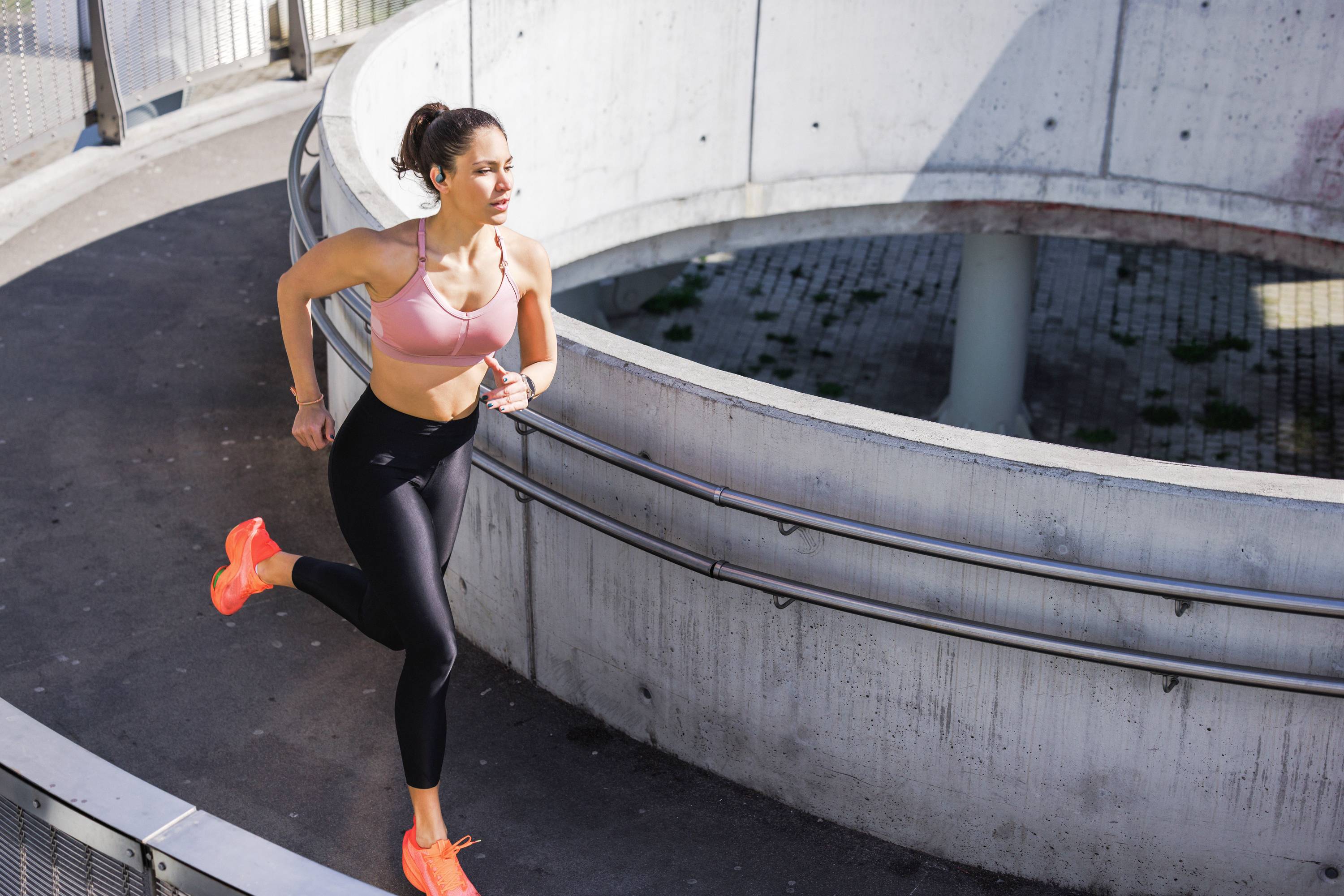 Frau joggt im Freien auf einer spiralförmigen Rampe. Sie trägt orangefarbene Turnschuhe und Sportkleidung.