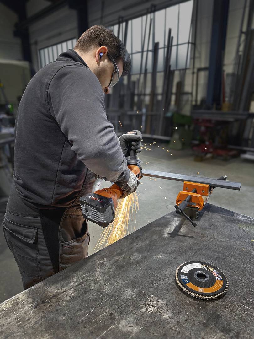 Ein Mann schneidet mithilfe eines Winkelschleifers Metall in einer Werkstatt. Funken fliegen vom Metallstück während des Schneidens.