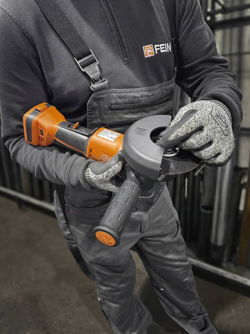 Person in Arbeitskleidung montiert eine Schleifscheibe auf einen Winkelschleifer, zeigt korrekten Umgang mit Werkzeug in einer Werkstatt.