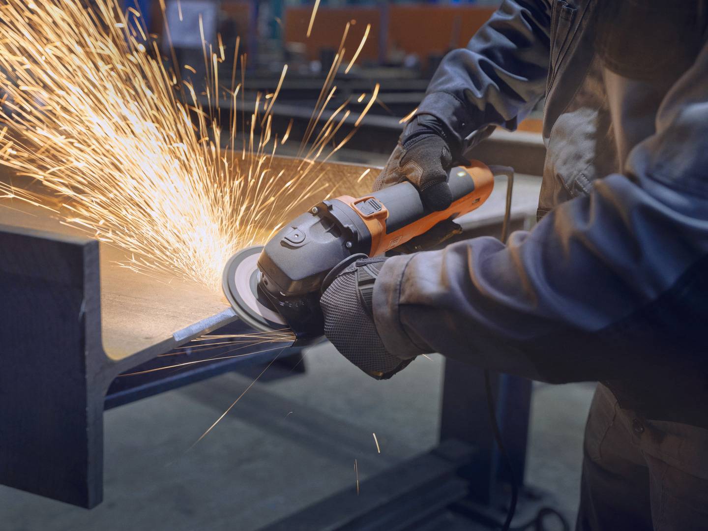 Person schleift Metall mit einer Winkelschleifmaschine, Funken fliegen. Arbeitet in einer Werkstatt oder Fabrik.