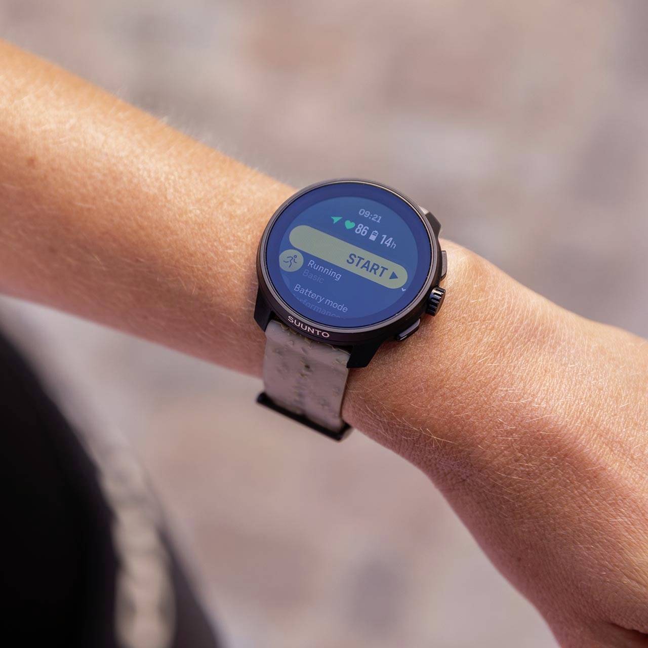 Eine schwarze Smartwatch an einem Handgelenk zeigt den Bildschirm mit einem blauen Start-Button und einer Fitness-App an.