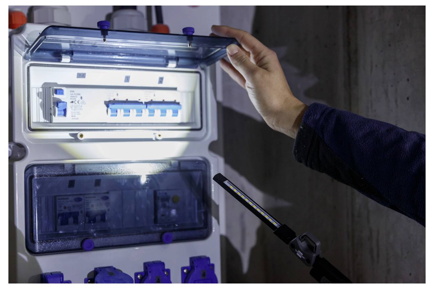 Person inspecting ein offenes Elektroverteilerpanel mit leuchtenden Schutzschaltern, während sie die Tür hält, was auf Wartungs- oder Installationsarbeiten hindeutet.