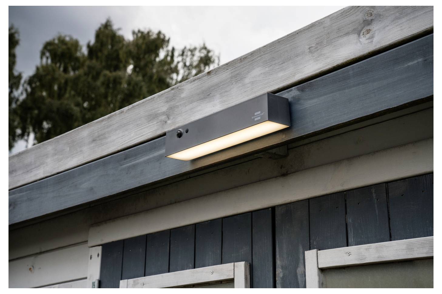 An der Wand montiertes Außenlicht unter einem Dachüberstand an einem dunklen Holzgebäude.