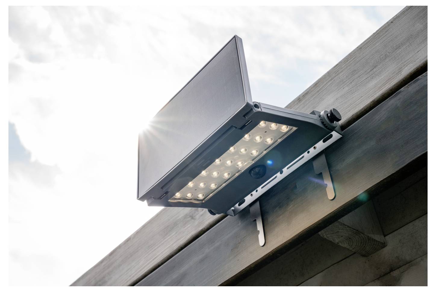 Außen angebrachter, an einer Dachrinne befestigter LED-Flutlichtstrahler, der im Winkel nach unten gegen einen hellen Himmel gerichtet ist.
