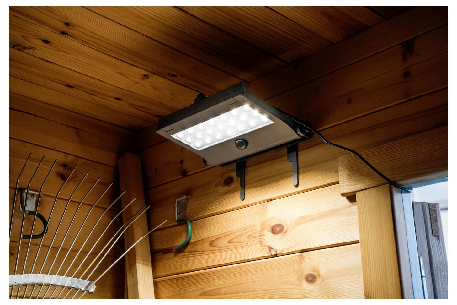 LED-Sicherheitsleuchte, die unter einem Holzdachüberstand montiert ist und den Wandbereich und den Eingangstürbereich im Freien beleuchtet.