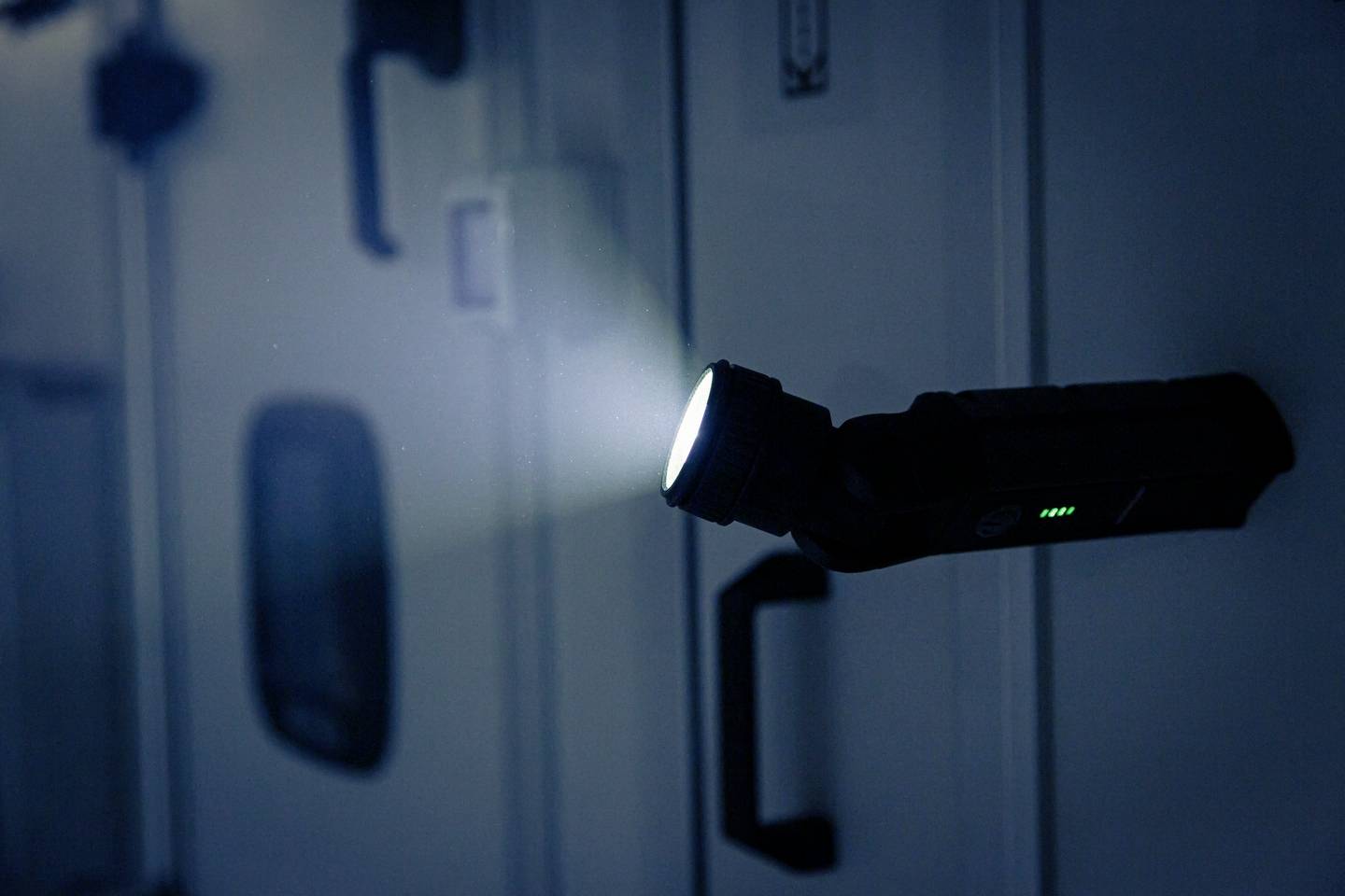 Taschenlampe leuchtet in dunklem Raum und beleuchtet Wand mit Griffen, die in einem Fahrzeug oder technischen Bereich sein könnten.