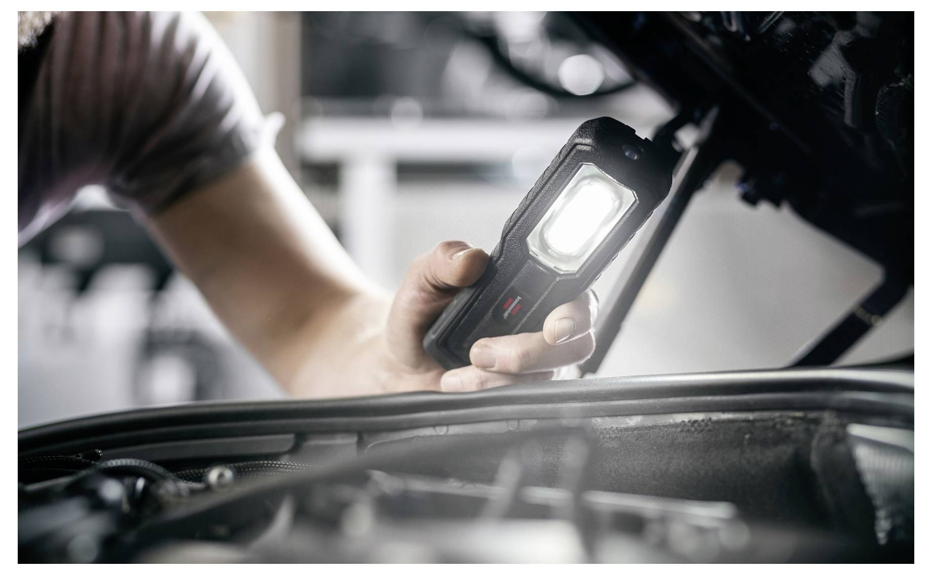 Mechaniker untersucht ein Automotor-Abteil mit einer tragbaren Inspektionsleuchte aus nächster Nähe.