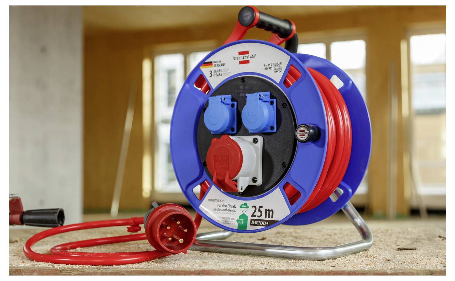 Tragbare elektrische Kabelrolle mit blauem und rotem Gehäuse, rotes Verlängerungskabel aufgerollt auf dem Boden, gekennzeichnet mit 25 m.