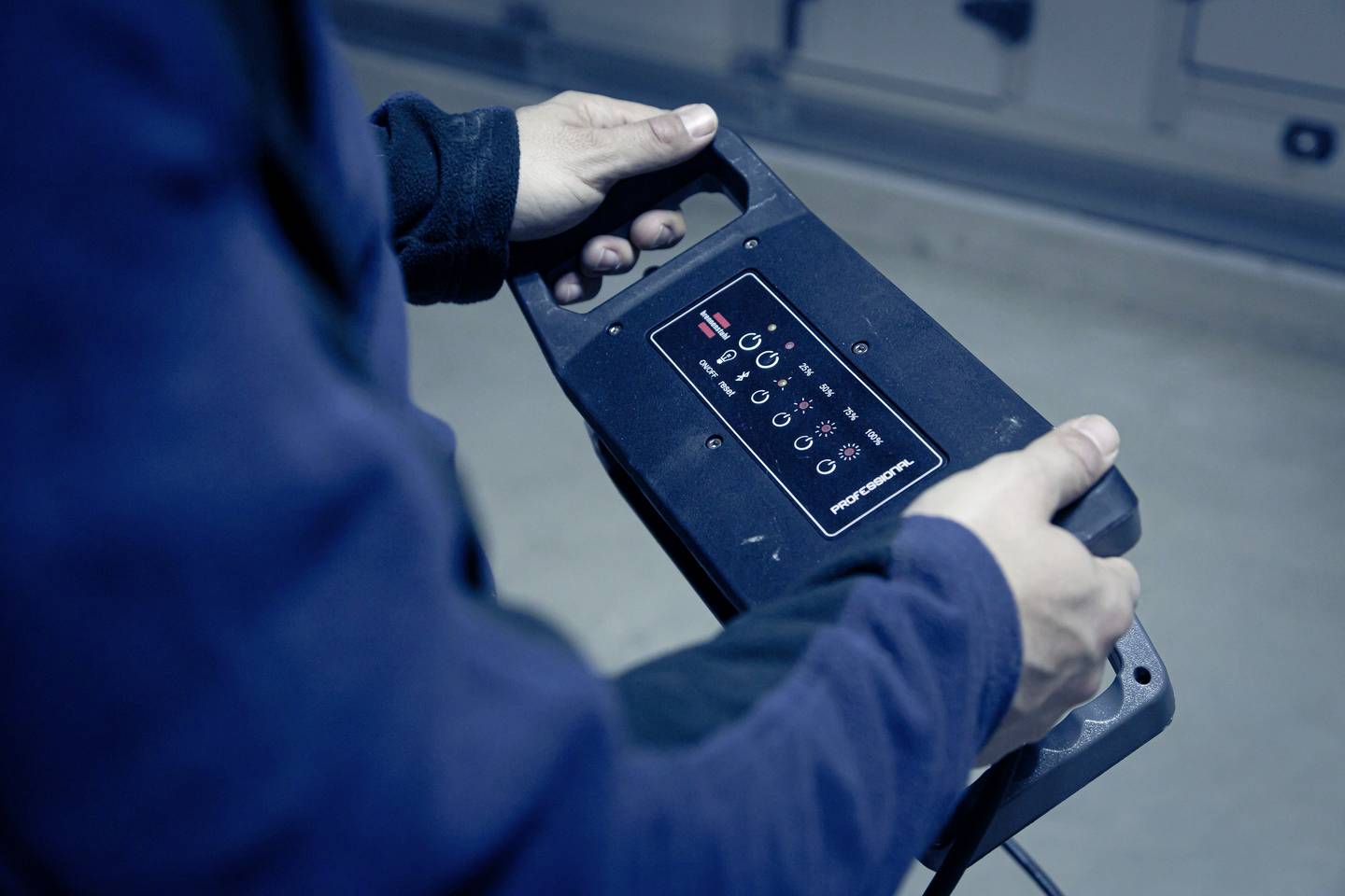 Eine Person hält ein elektronisches Steuergerät mit mehreren Knöpfen und Anzeigelichtern in der Hand.