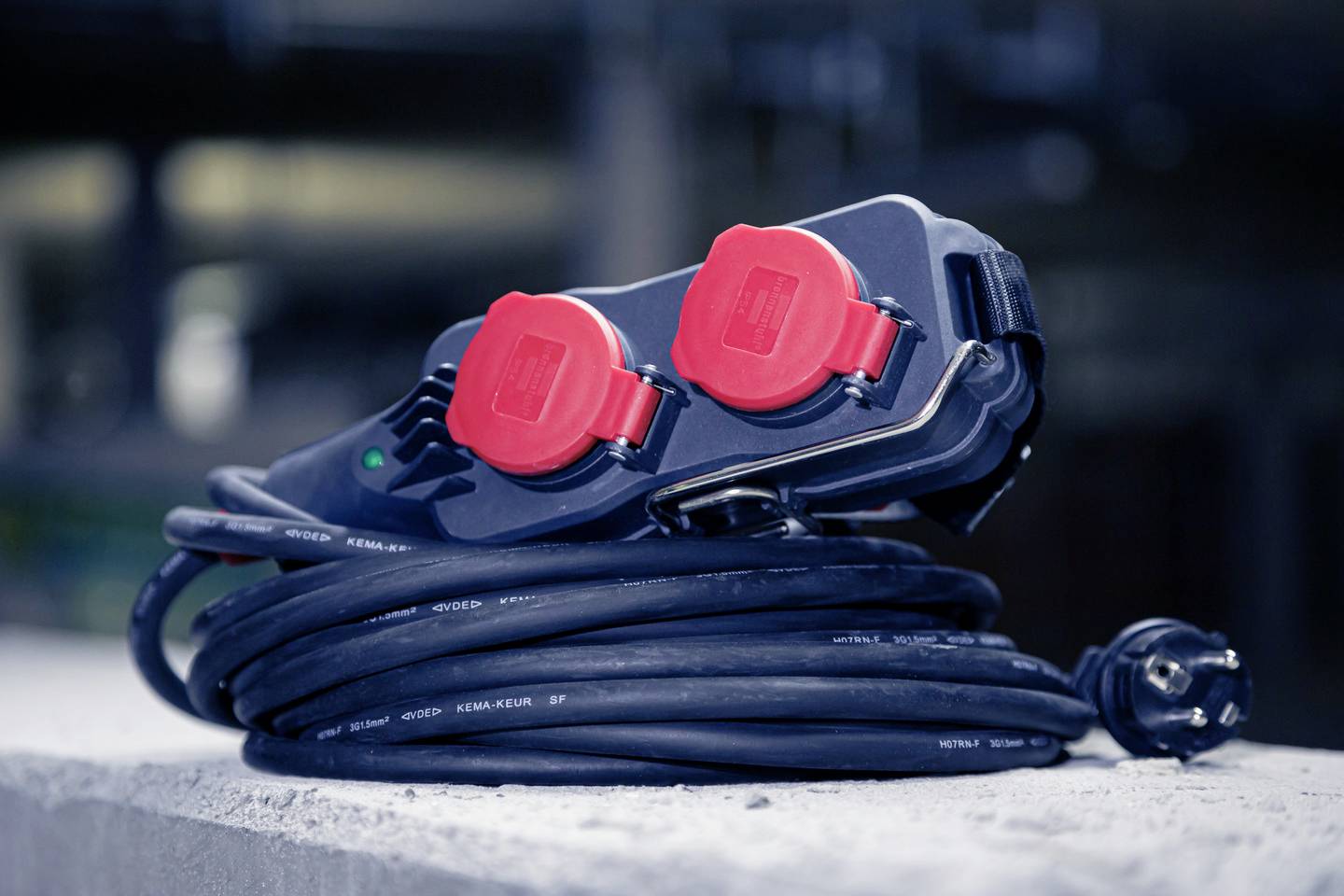 Ein zusammengerolltes schwarzes Verlängerungskabel mit rotem Stecker auf einer Betonfläche, Symbol für Elektrizität und Werkzeugeinsatz.