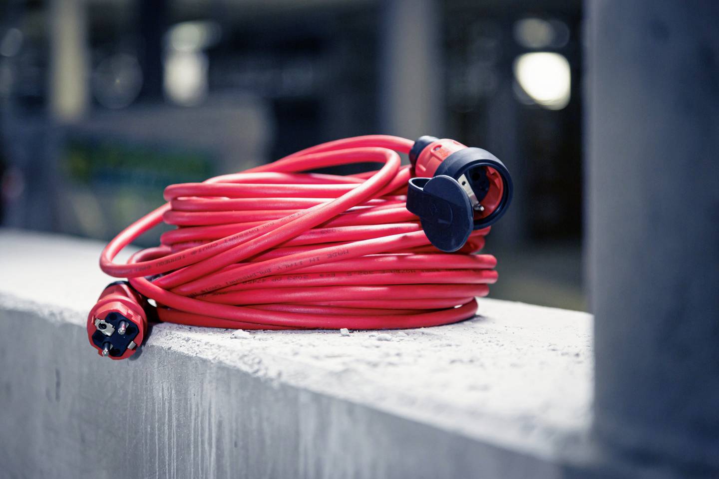 Ein aufgerolltes, rotes Verlängerungskabel liegt auf einer Betonfläche.