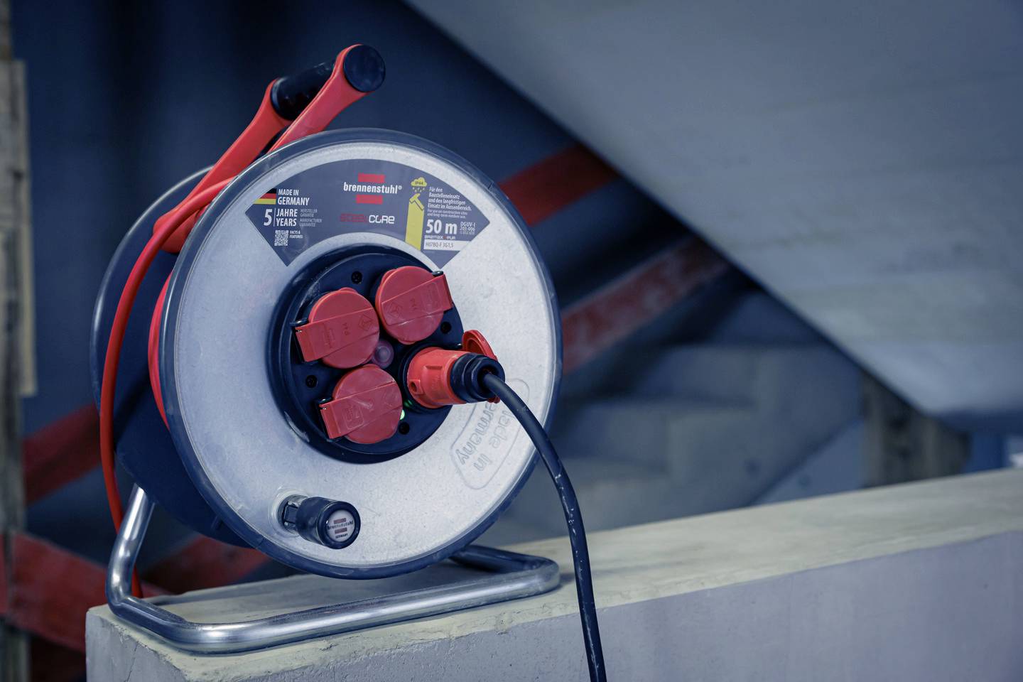 Eine Kabeltrommel mit mehreren Steckdosen und einem Verlängerungskabel steht auf einem Betonblock in einem industriellen Umfeld.
