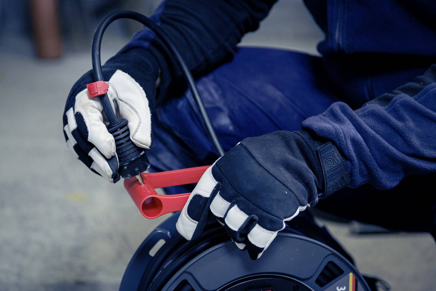 Eine Person führt eine Kabelreparatur durch. Sie hält ein Kabel mit roten Klemmen, während sie mit schwarzer Arbeitshandschuhen arbeitet.