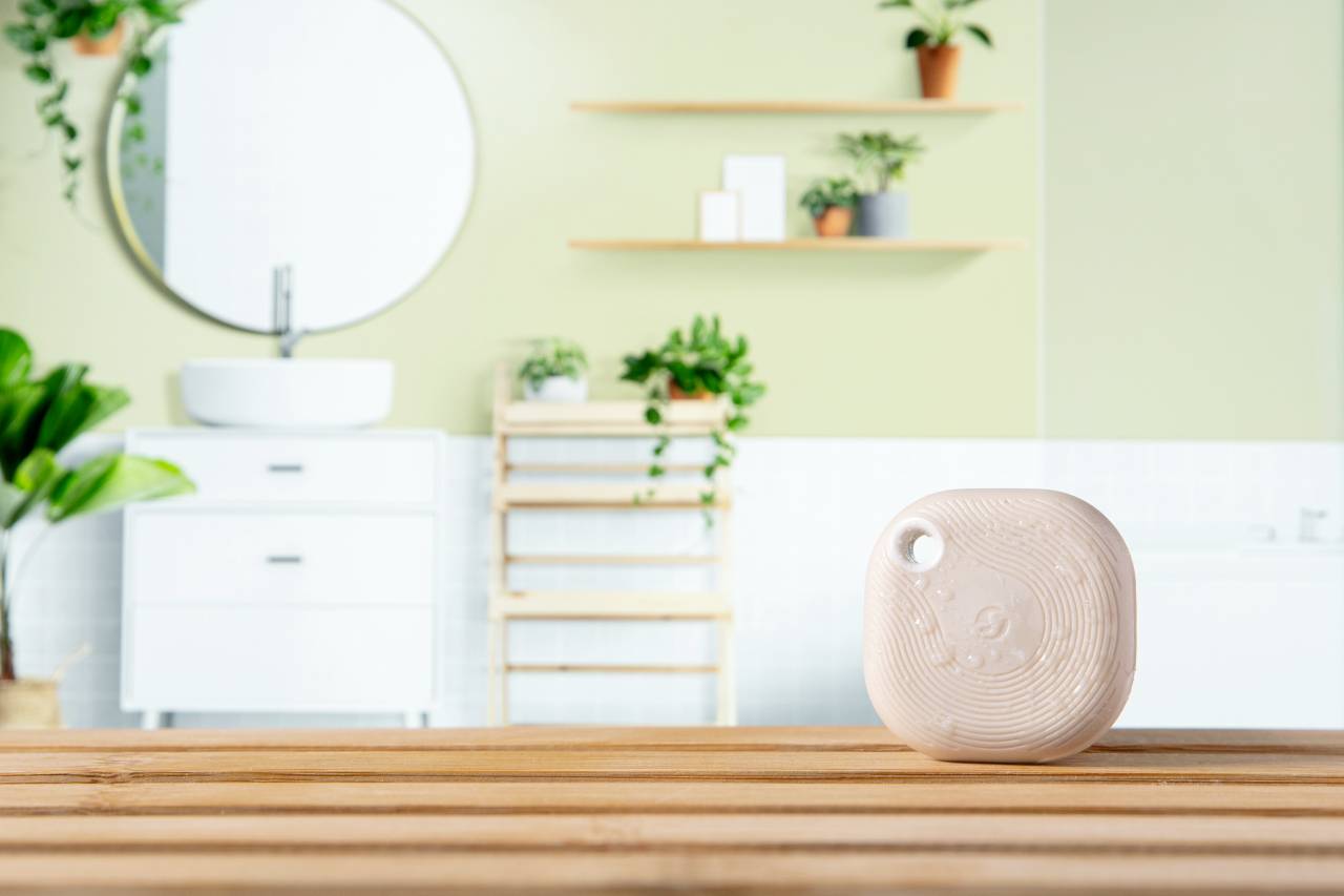 Kleine weiße Fliese mit Rillenmuster auf hölzerner Oberfläche in modernem Badezimmer mit Pflanzen und Spiegel im Hintergrund.