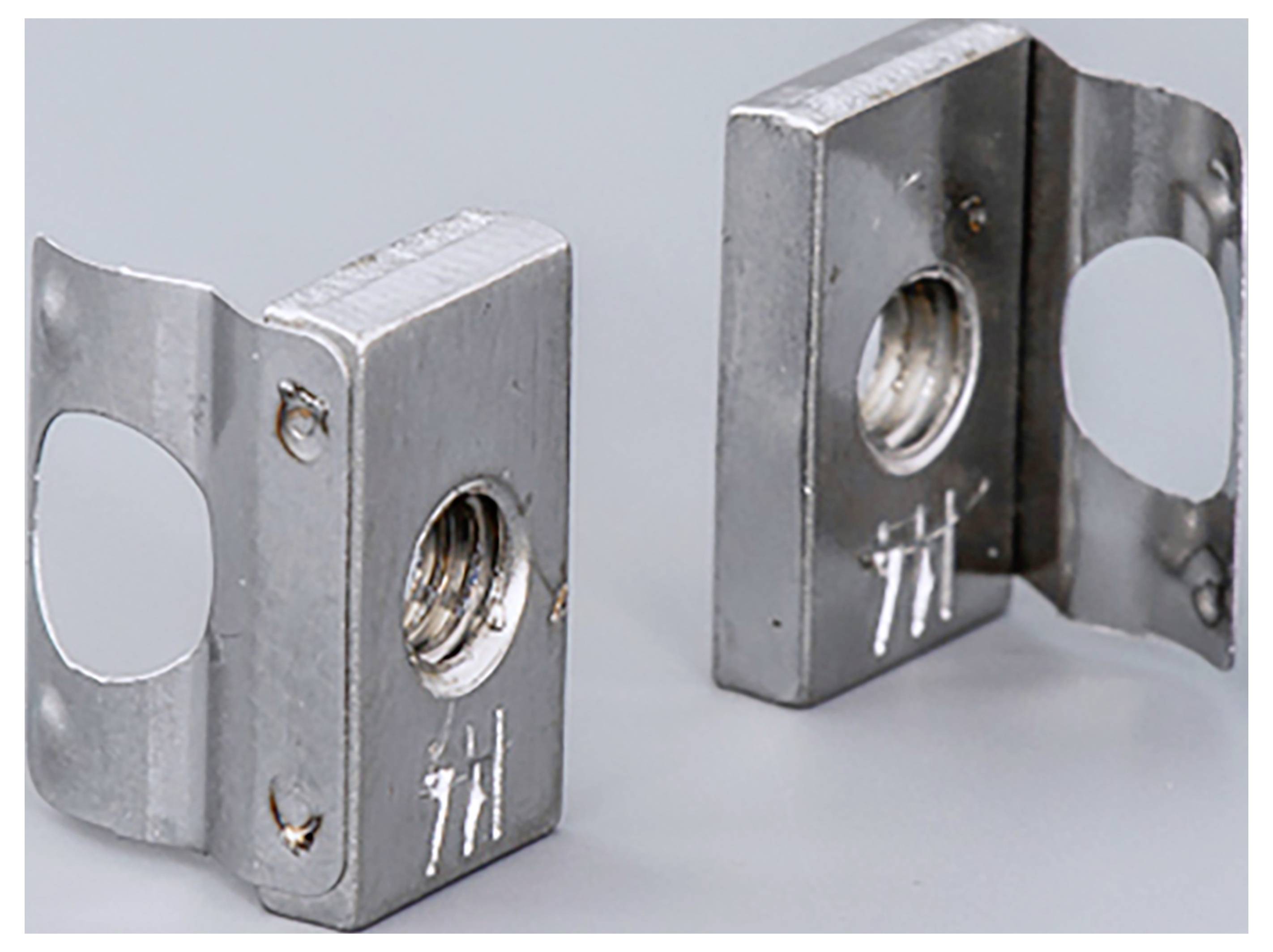 Zwei metallische Halterungen mit quadratischem Design und Gewindelöchern, stehen aufrecht auf einer grauen Oberfläche.