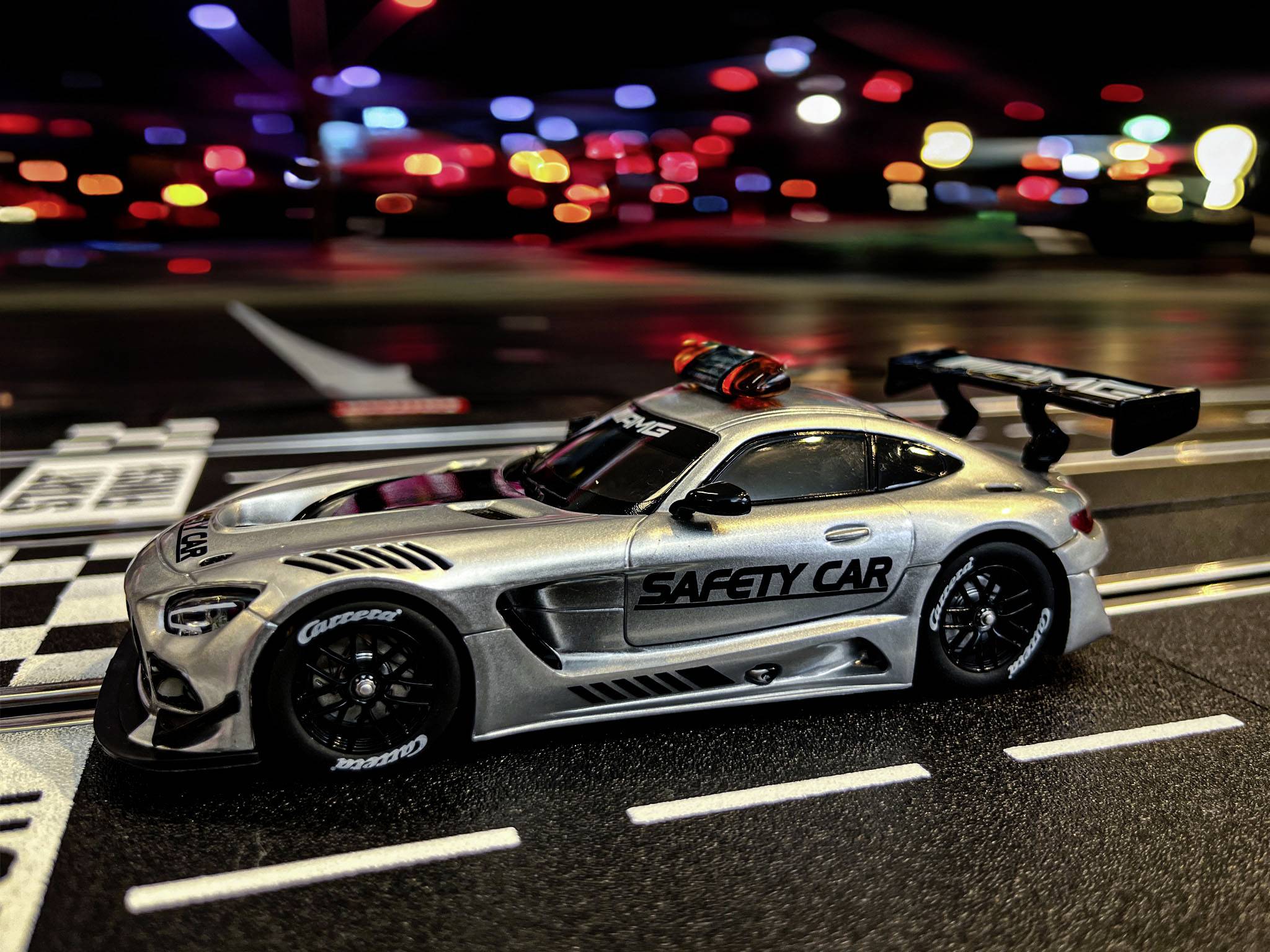 Spielzeug-Sicherheitsauto auf einer Autorennbahn mit bunten Lichtern im Hintergrund.