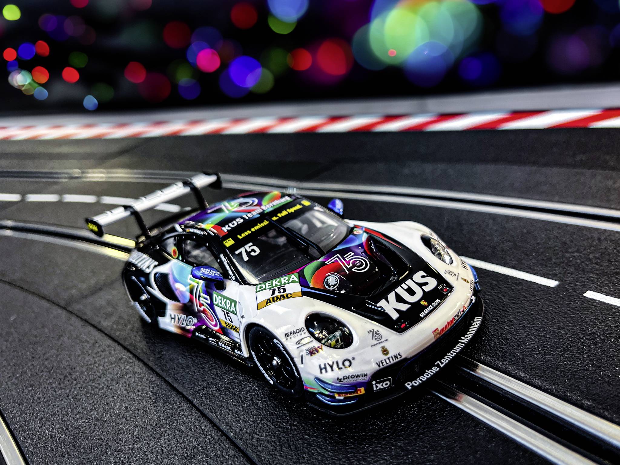 Rennwagen auf einer Carrera-Rennbahn mit bunter Beleuchtung im Hintergrund. Das Auto trägt die Nummer 75 und Sponsorenlogos.