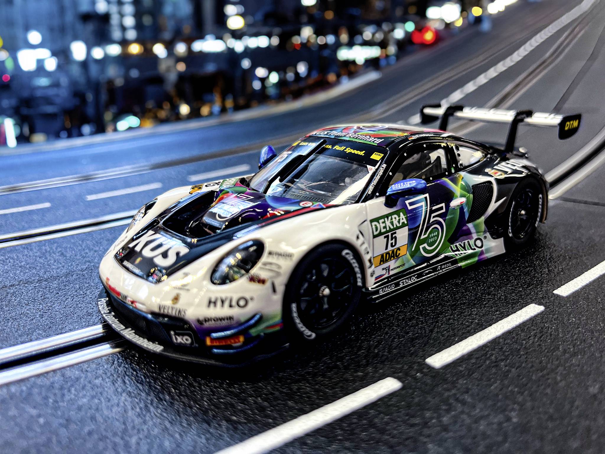 Ein Modellauto eines Rennwagens auf einer Streckensimulation in Miniaturansicht, im Hintergrund sind unscharfe Stadtlichter zu sehen.