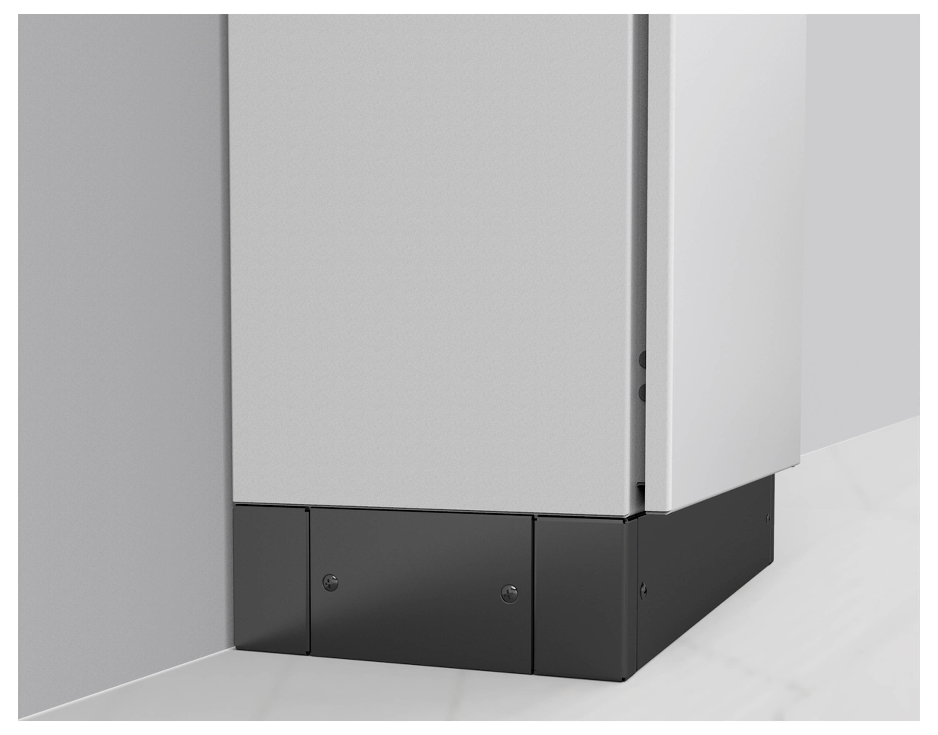 Ein schmaler, grauer Eckschrank mit einer glatten Oberfläche. Unten ist ein schwarzer Sockel. Der Schrank steht an der Wand.