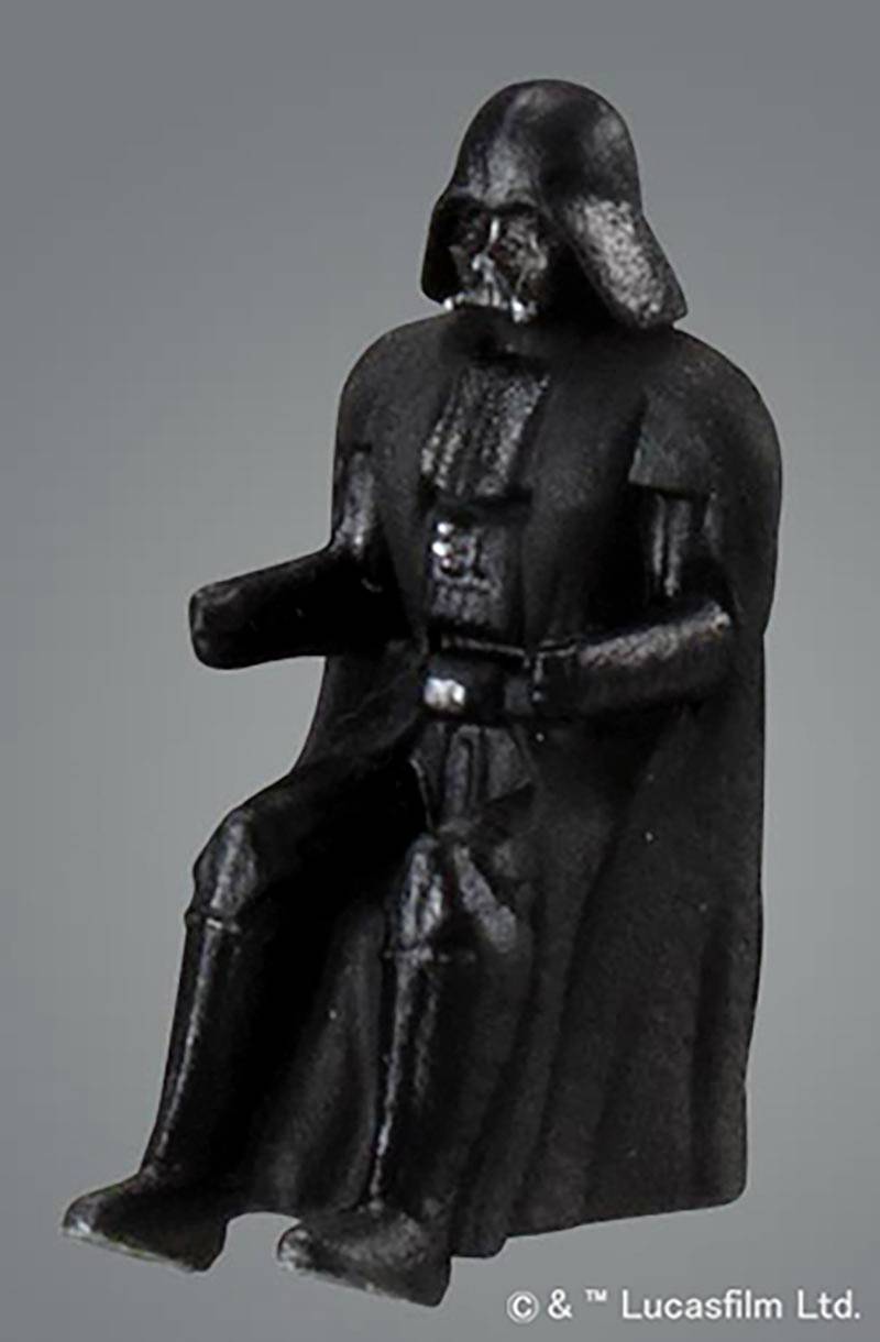 Schwarze Plastikfigur einer Person mit Helm und Umhang, in sitzender Haltung.