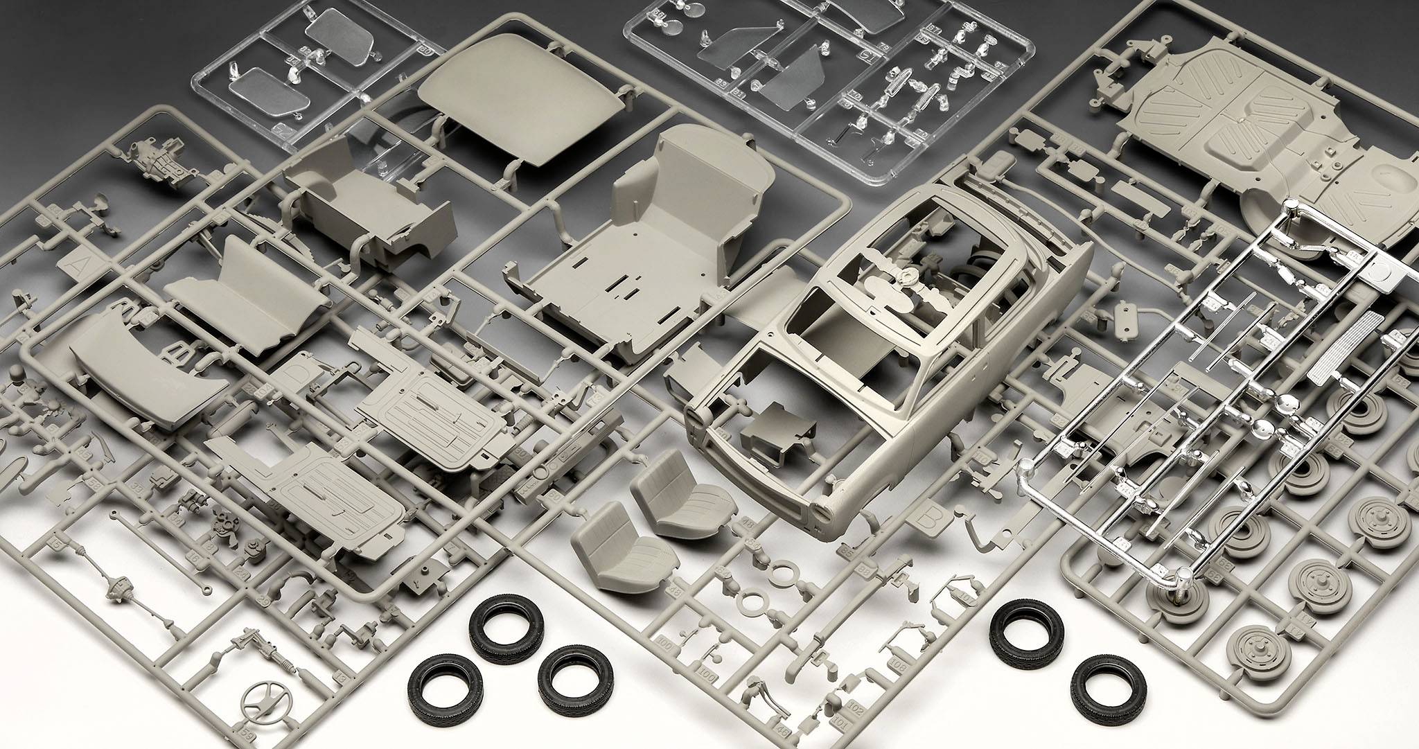 Mehrere Plastikrahmen mit Teilen eines Modellauto-Bausatzes, darunter Karosserie, Sitze und Reifen, auf flacher Oberfläche ausgebreitet.