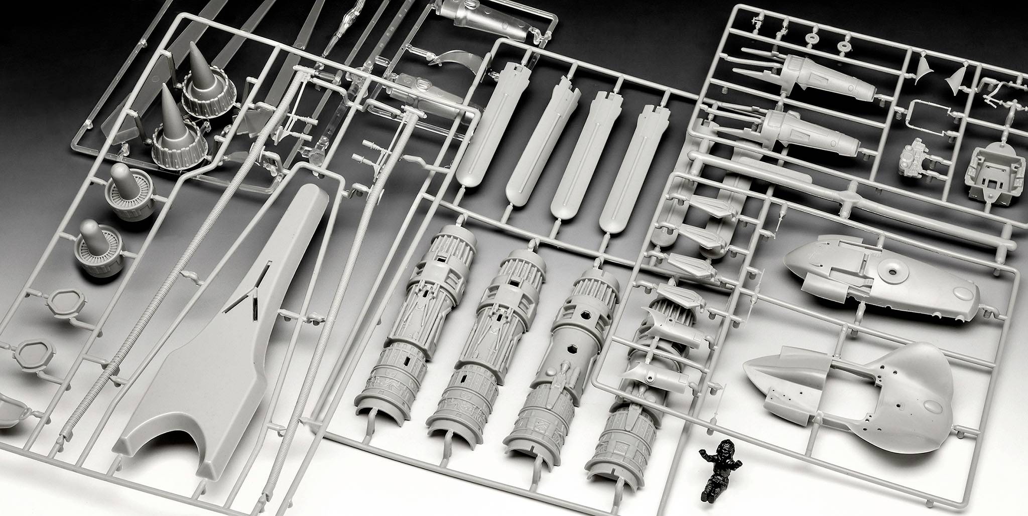 Bausatz aus grauem Kunststoff mit zahlreichen Einzelteilen für den Zusammenbau eines Modells, darunter Flügel, Düsen und Figuren.