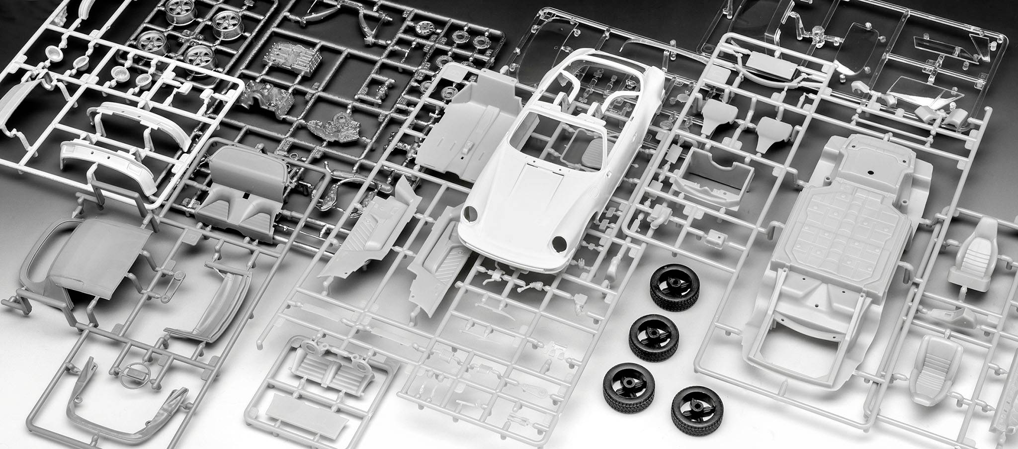 Teile eines Modellauto-Bausatzes, die einen zusammengebauten Sportwagen darstellen, liegen geordnet auf einer Fläche.