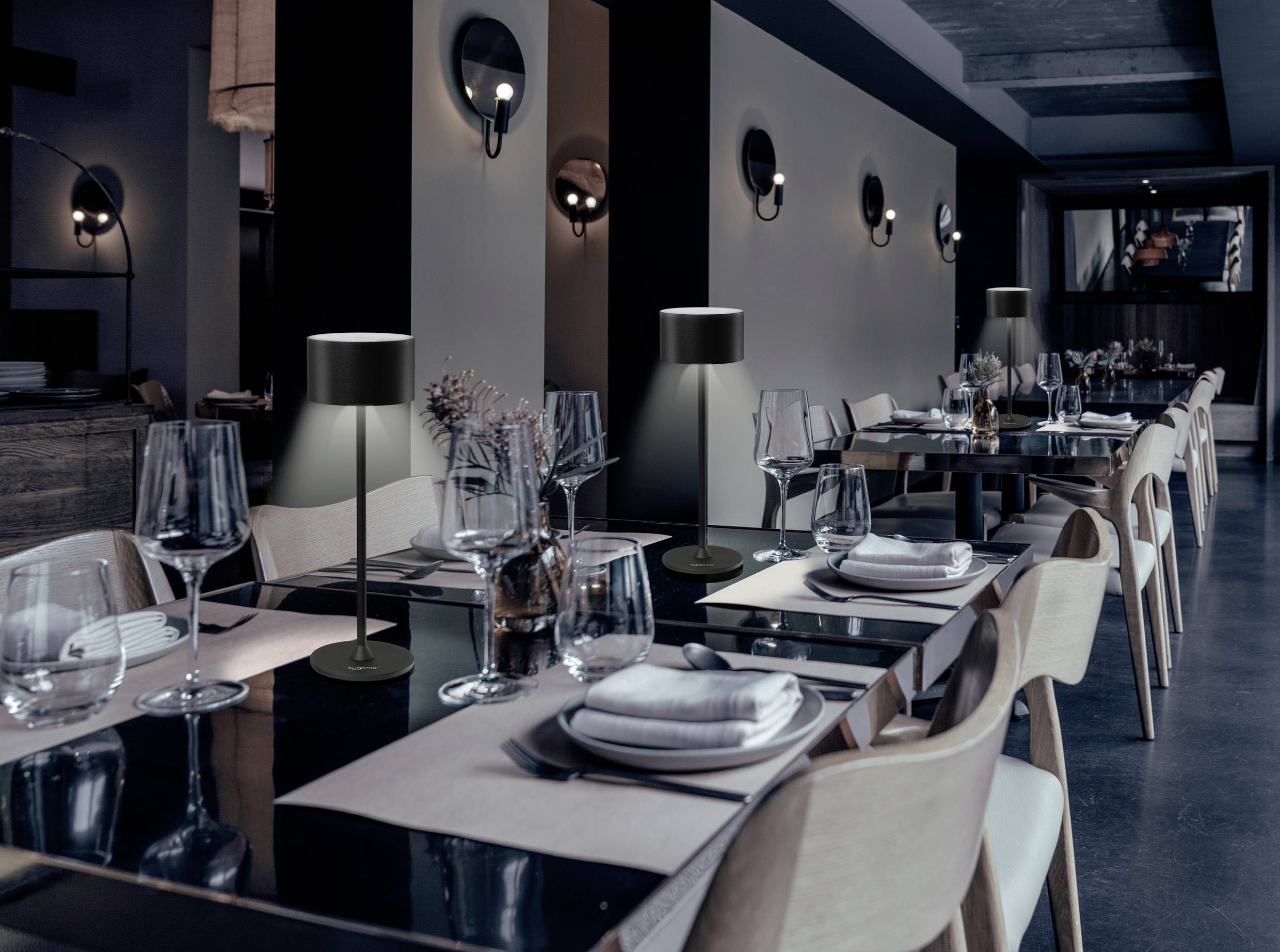 Ein elegant gedeckter Restauranttisch mit weißen Servietten, Weingläsern und modernen Tischlampen.