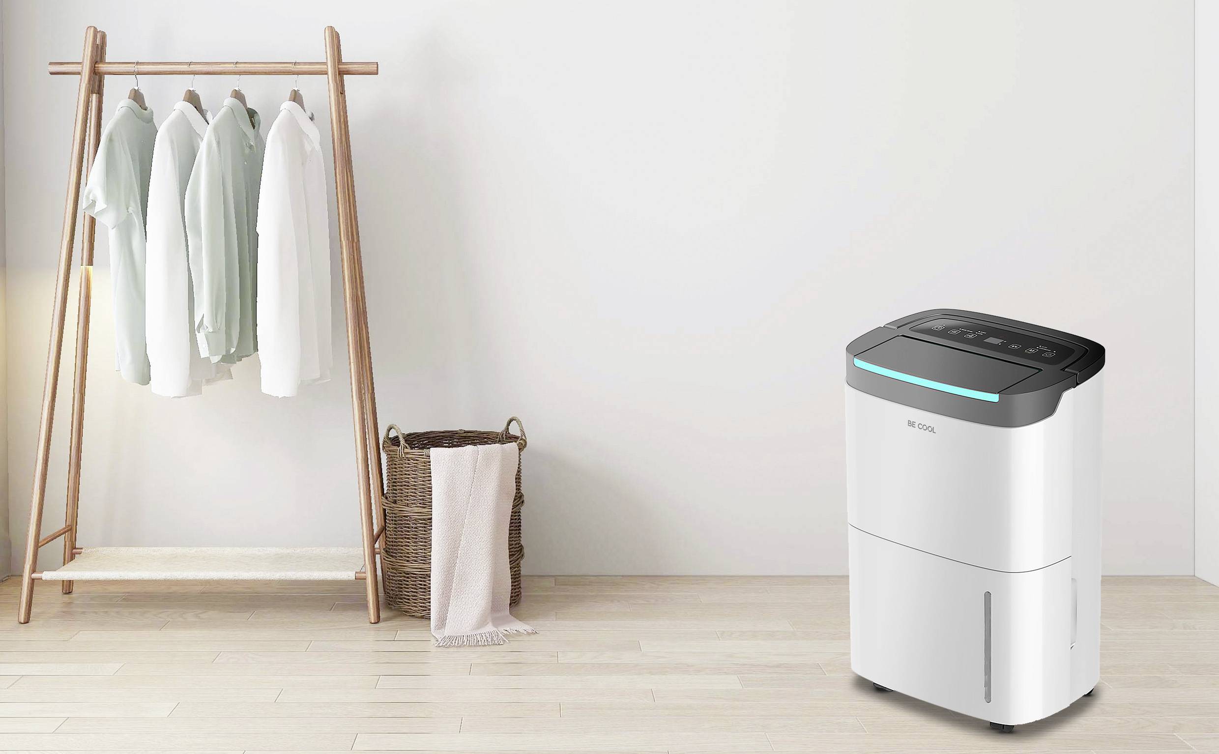 Ein moderner Luftentfeuchter steht in einem hellen Raum neben einem Holzständer mit hängenden Hemden und einem geflochtenen Korb.