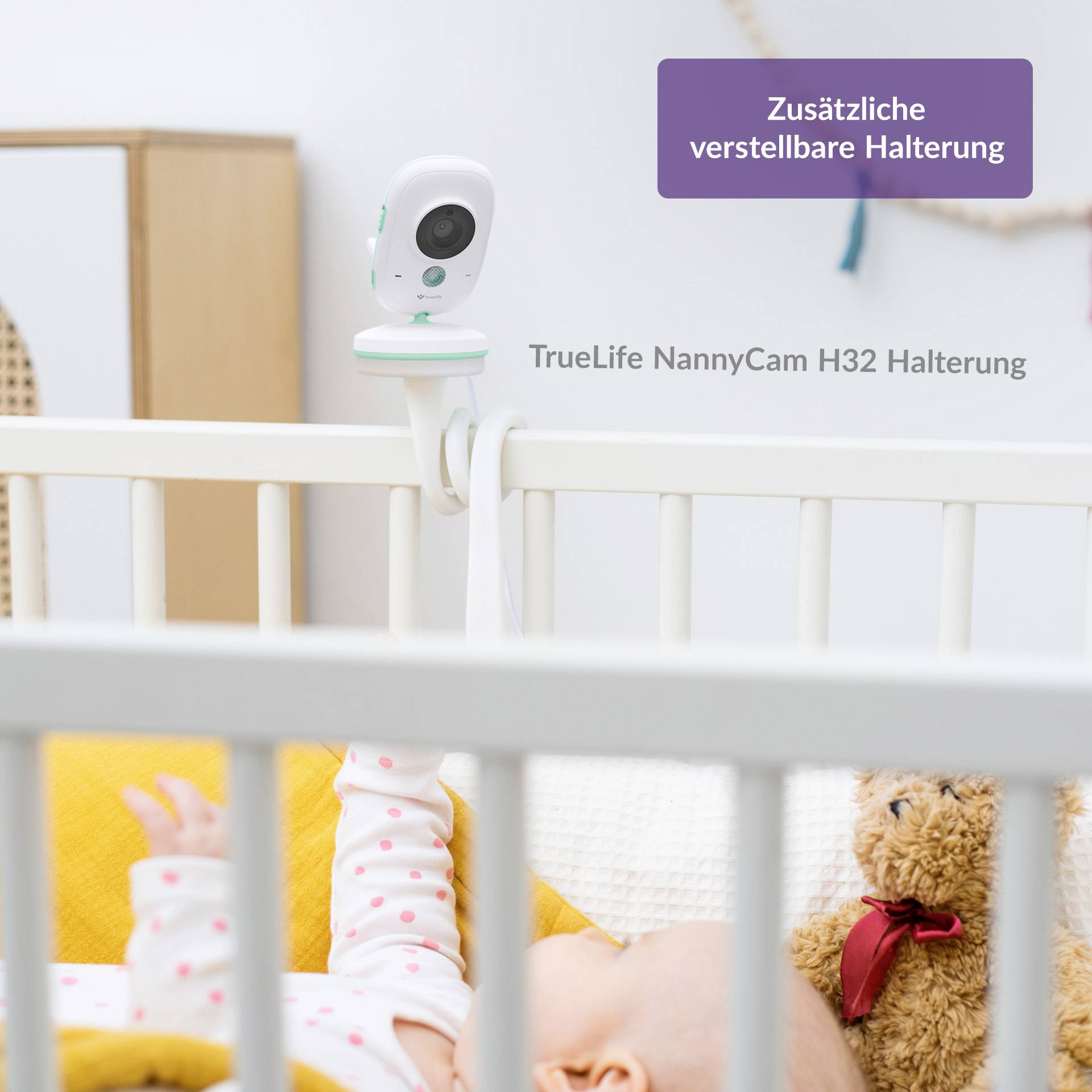 Eine Babycam mit verstellbarer Halterung ist an einem Kinderbett befestigt. Ein Baby liegt im Bett, teilweise verdeckt von Decke und Kuscheltier.