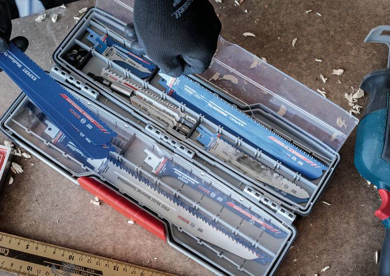 Sägeblätter-Set in einem offenen Kunststoffkoffer. Eine behandschuhte Hand hält ein Blatt. Verschiedene Größen und Typen sind sichtbar.