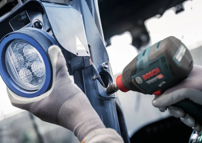 Eine Person montiert mit einem Akkuschrauber ein blau umrandetes Licht an eine Metallstruktur. Die Person trägt Arbeitshandschuhe.