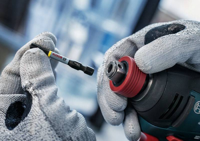 Eine Person hält einen Akkuschrauber mit Handschuhen und setzt einen Bosch-Bit ein.