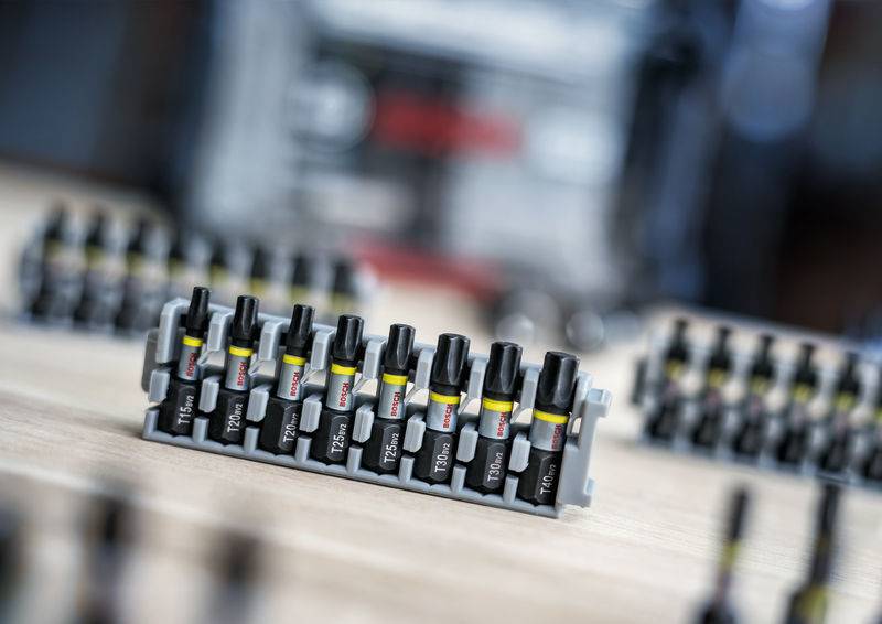 Mehrere schwarze Schraubendrehereinsätze sind in einem Kunststoffhalter auf einem Holztisch angeordnet. Im Hintergrund unscharf.