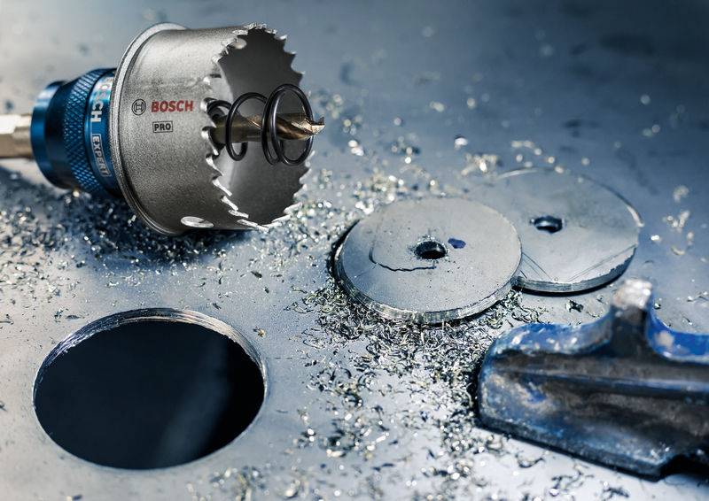 Bohrkrone von Bosch liegt auf Metalloberfläche, umgeben von Metallspänen und ausgeschnittenen Metallkreisen. Hauptinformation: Anwendung im Metallbohren.