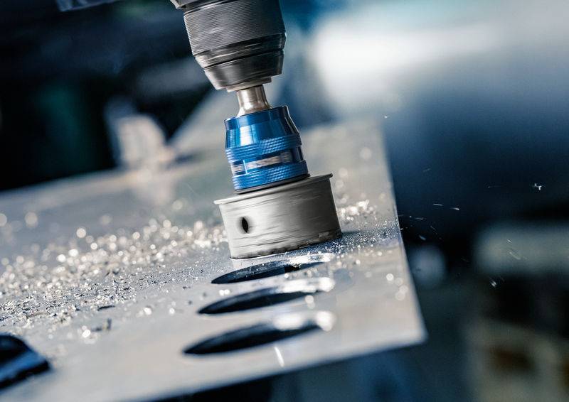 Nahaufnahme eines Bohrers, der ein rundes Loch in ein Metallblech bohrt. Metallspäne sind sichtbar.