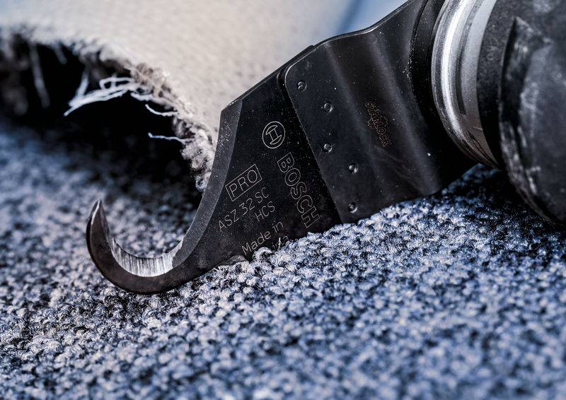 Nahaufnahme einer Bosch-Werkzeugklinge, die Teppichboden durchschneidet. Teile des Teppichs sind fransig und aufgeraut.