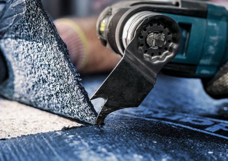 Eine Person verwendet ein elektrisches Werkzeug, um Dachmaterial zuzuschneiden. Das Werkzeug schneidet durch eine Schicht Dachschindeln.