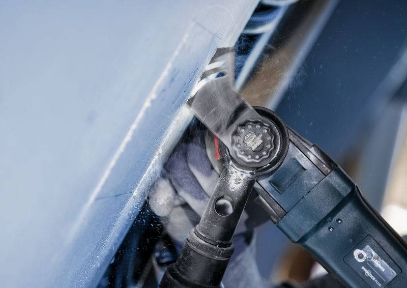 Eine Person verwendet ein elektrisches Werkzeug, um ein blaues Metallstück zu bearbeiten. Späne und Funken sind sichtbar.