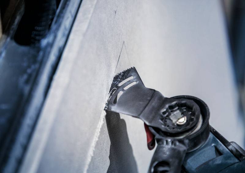 Eine elektrische Säge schneidet in eine Trockenbauwand. Der Sägekopf ist scharf fokussiert, während die Umgebung unscharf ist.