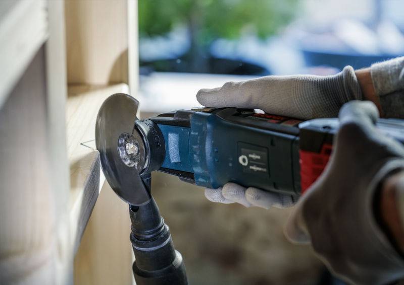 Eine Person mit Handschuhen nutzt ein elektrisches Schneidwerkzeug, um ein Holzstück zu bearbeiten.