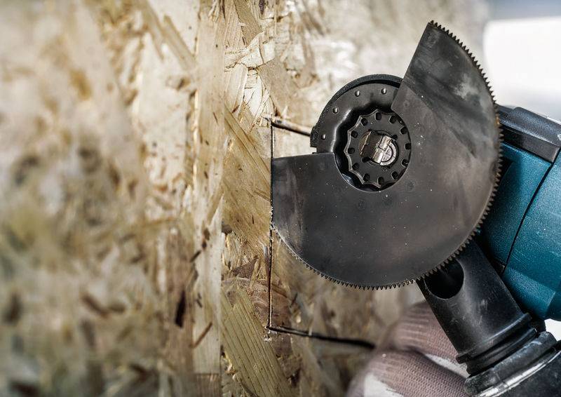 Eine Person schneidet mit einem Winkelschleifer ein hartes Material, möglicherweise Holz oder Pressspanplatte. Werkzeug und Struktur sind sichtbar.