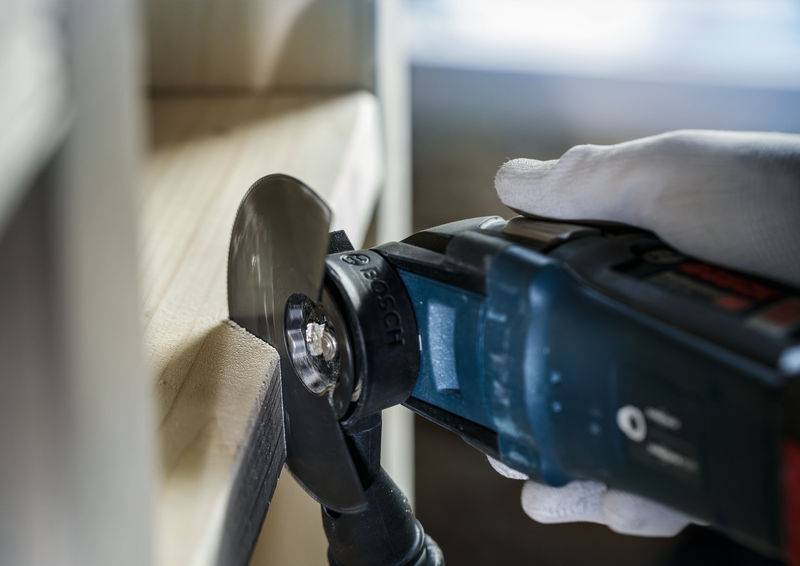 Eine Person schneidet mit einem Multifunktionswerkzeug aus Metall an einer Holzkante.