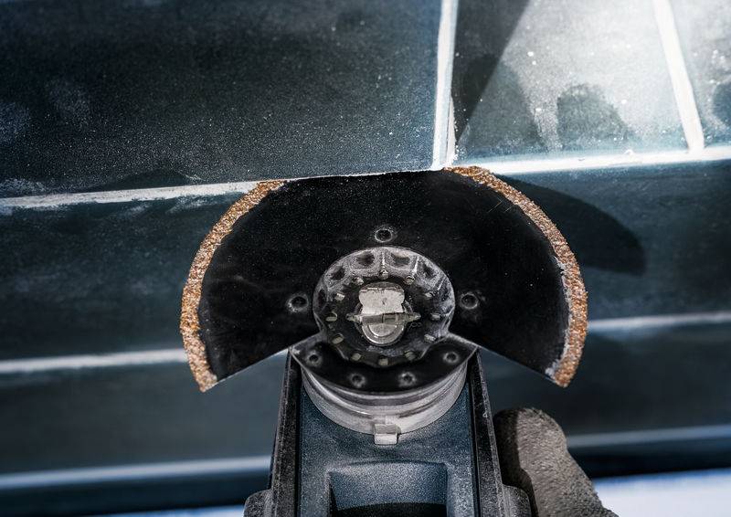 Eine Flexschleifertrennscheibe schneidet durch eine Keramikfliese. Ein Schutzhandhandschuh hält das Werkzeug sicher, während der Schnitt erfolgt.