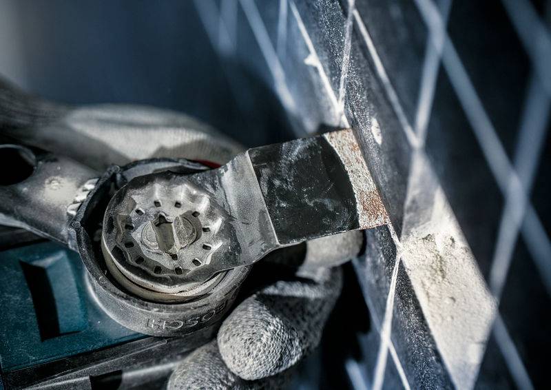 Eine handgehaltene oszillierende Säge wird verwendet, um Fliesen zu schneiden. Eine Person trägt Handschuhe und arbeitet an einer Wand.