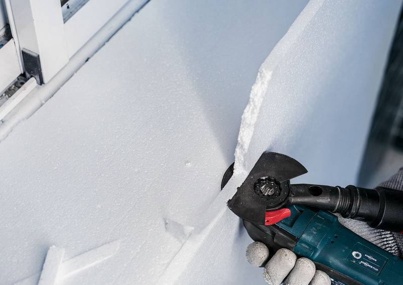 Ein Handwerker schneidet mit einem Winkelschleifer eine dicke Styroporplatte an einer Wand. Der Fokus liegt auf der Präzisionsarbeit.