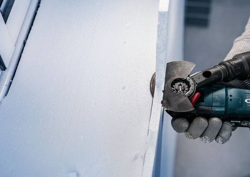 Eine Person benutzt ein elektrisches Werkzeugs, um die Kante einer weißen, schaumstoffähnlichen Oberfläche zu schneiden.