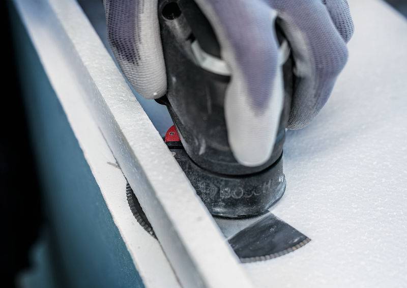 Eine Elektrosäge schneidet durch ein weißes Material, wobei eine Person schützende Handschuhe trägt.