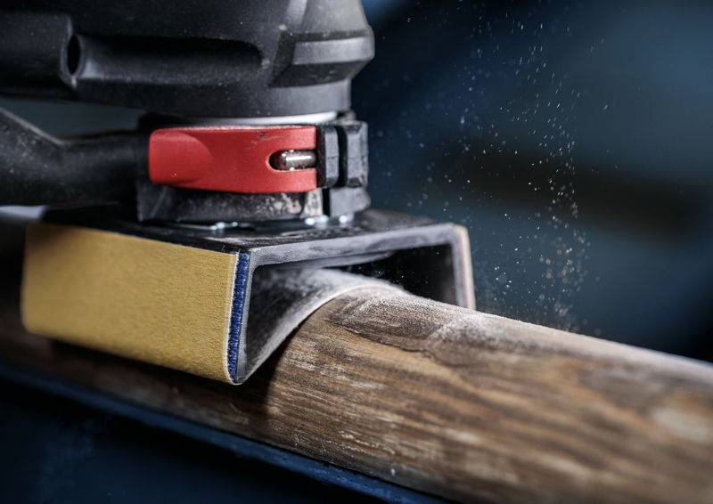 Schleifmaschine glättet ein Holzstück, sichtbarer Staub in der Luft, Nahaufnahme.